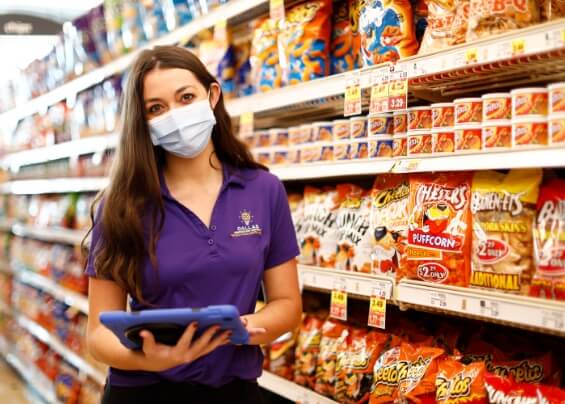 Woman worker wearing a mask in a supermarket in front of PepsiCo snacks bags, using a tablet